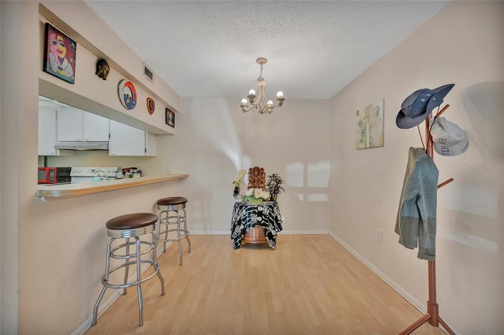 A dining area features light wood flooring, a breakfast bar with stools, and a chandelier — 3221 BENEVA ROAD UNIT 102, SARASOTA, FL