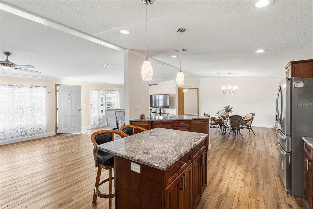 An open-concept kitchen features a granite-topped island, dark wood cabinetry, and light wood flooring — 5230 REVELATION DRIVE, POLK CITY, FL