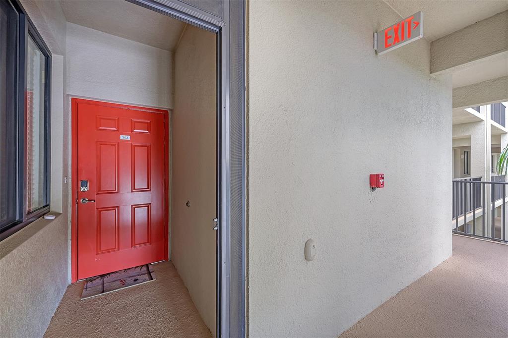 An exterior view of an apartment entrance with a bright red door and a screen door — 7121 RIVER HAMMOCK DRIVE UNIT 302, BRADENTON, FL