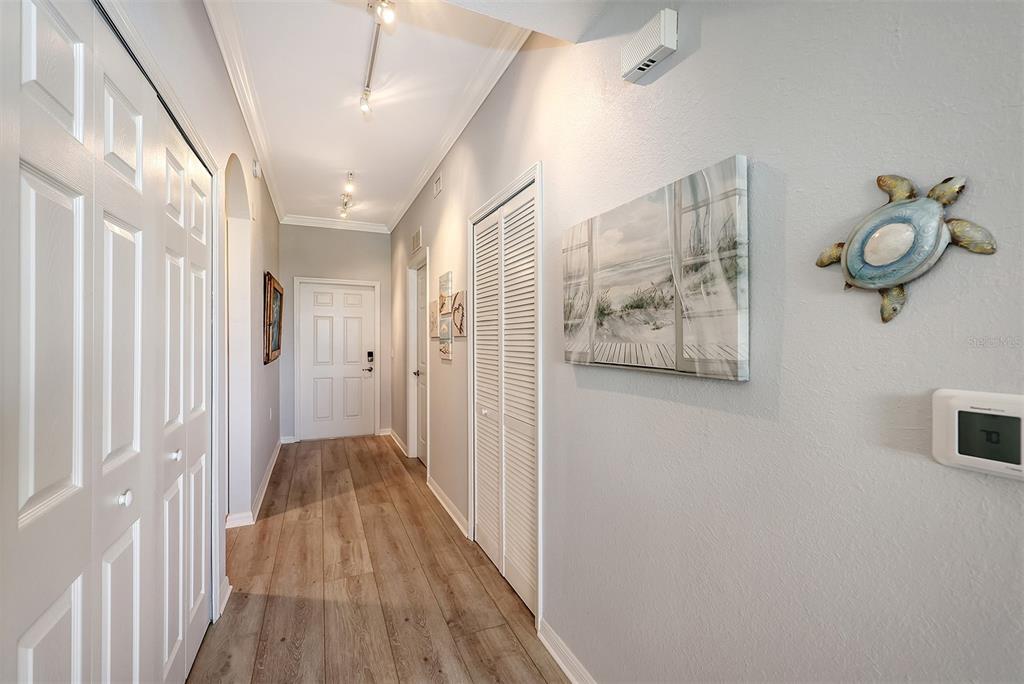A hallway with light wood flooring, white paneled doors, and coastal wall decor — 7121 RIVER HAMMOCK DRIVE UNIT 302, BRADENTON, FL