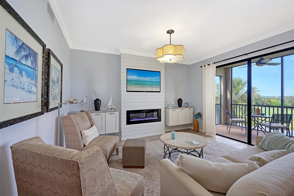 A living room features a fireplace, wall-mounted television, and sliding glass doors to a balcony — 7121 RIVER HAMMOCK DRIVE UNIT 302, BRADENTON, FL