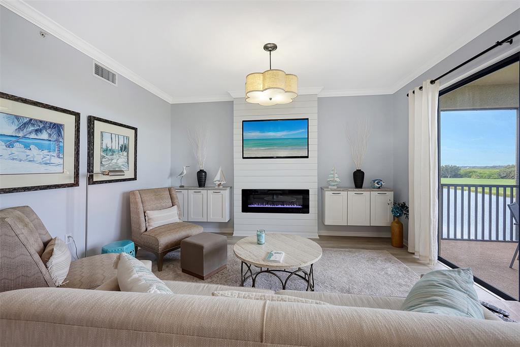 A living room features a fireplace, wall-mounted television, neutral furniture, and a balcony with water views — 7121 RIVER HAMMOCK DRIVE UNIT 302, BRADENTON, FL