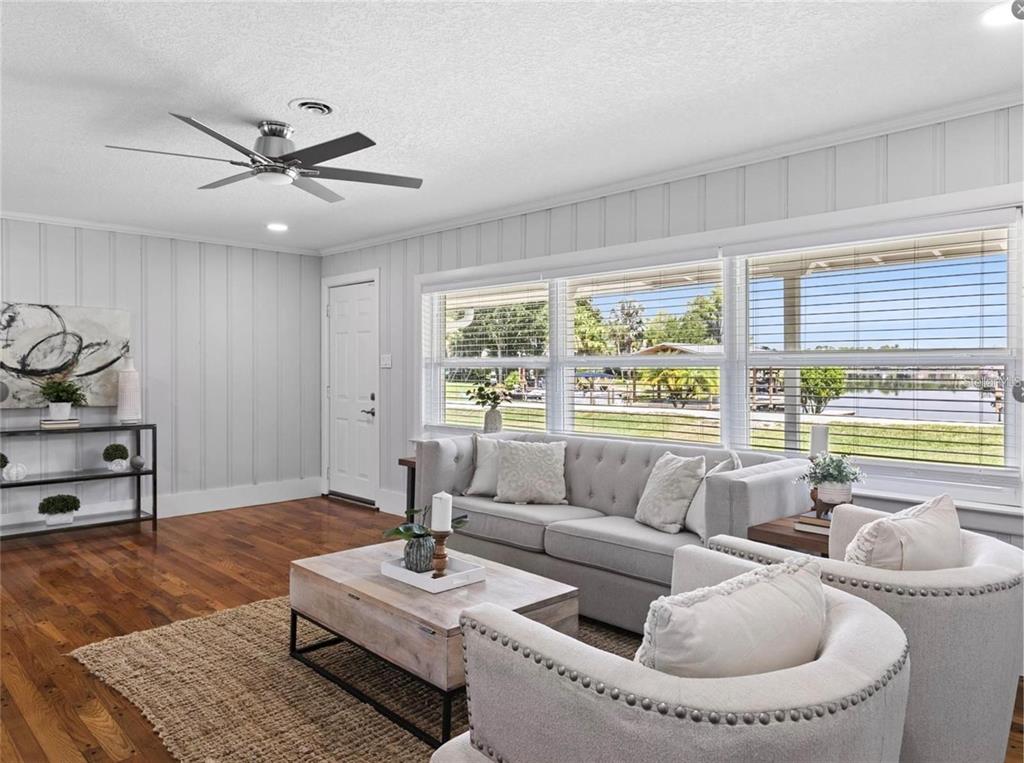 A living room with light gray walls, wood floors, a gray sofa, and large waterfront windows — 212 W 1ST AVENUE, WINDERMERE, FL