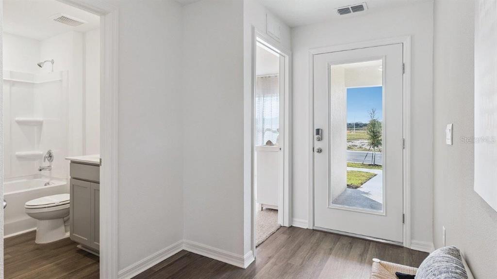 An entryway with wood-look flooring leads to a bathroom and a door with glass panels — 1126 AMBERS WAVE COURT, LAKE WALES, FL