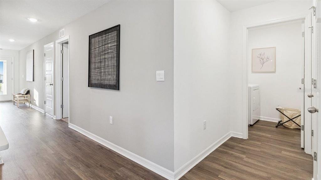 A hallway with wood-look flooring leads to a laundry room and other interior doors — 1126 AMBERS WAVE COURT, LAKE WALES, FL