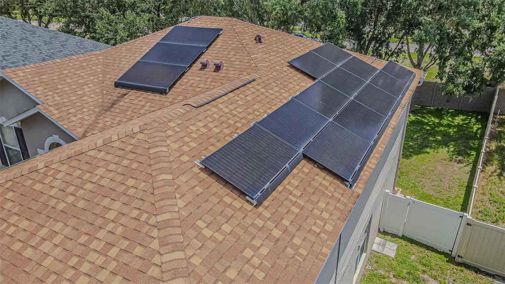 An aerial view of a shingled residential roof featuring two separate arrays of solar panels — 2706 MINGO DR, LAND O LAKES, FL
