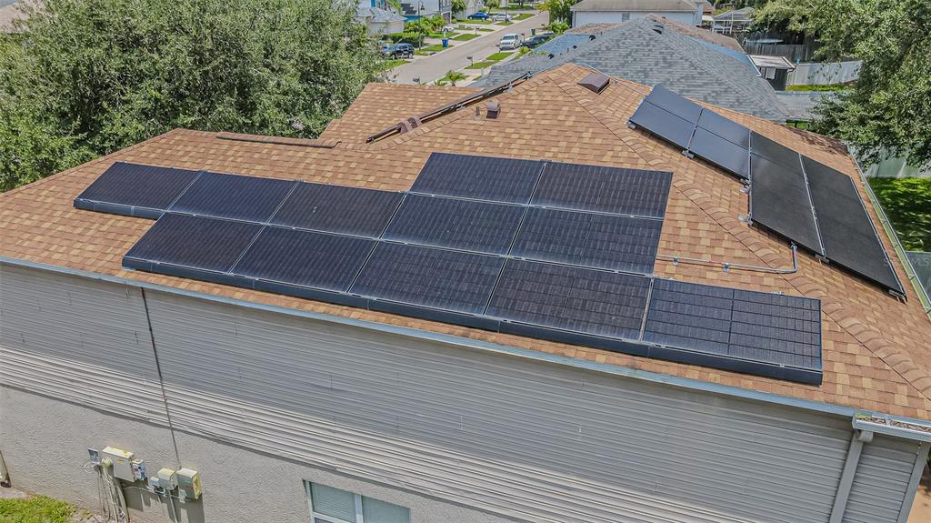 An aerial view of a shingled residential roof featuring two arrays of installed solar panels — 2706 MINGO DR, LAND O LAKES, FL