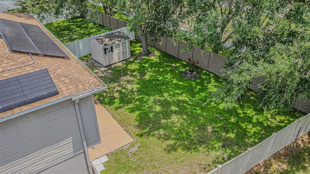 An aerial view of a backyard featuring a lawn, a storage shed, and solar panels — 2706 MINGO DR, LAND O LAKES, FL