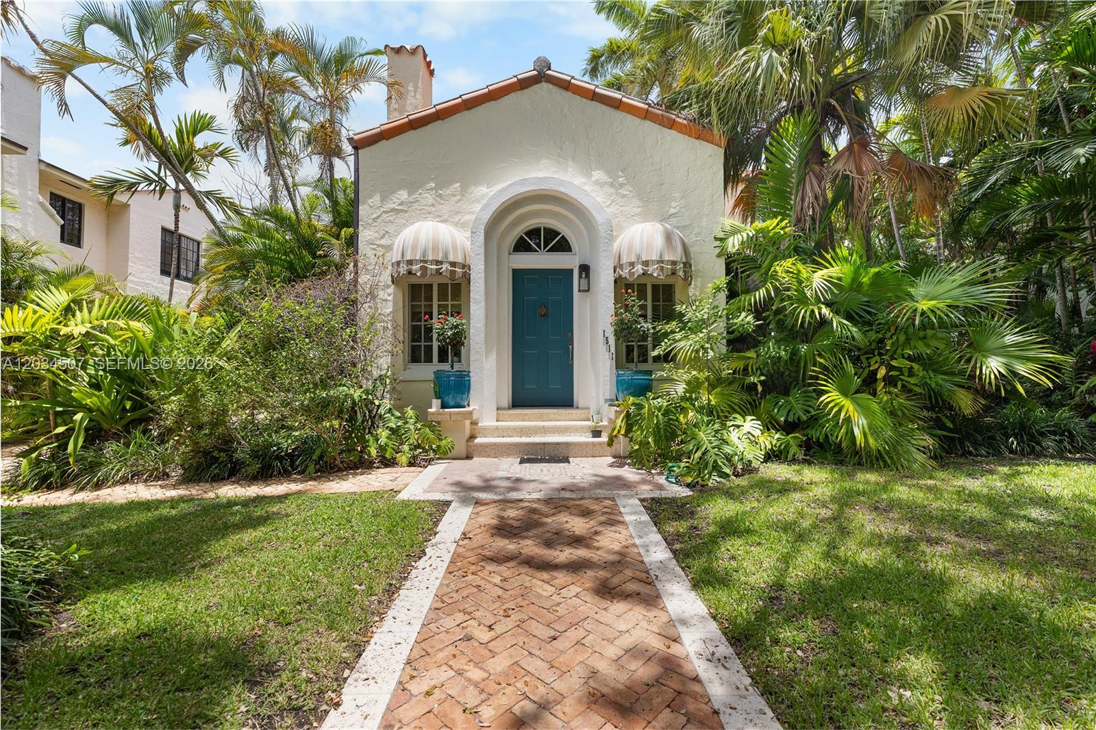A front view of a small, cream-colored stucco house with a blue door and awnings — 1511 SW 13th St, Miami FL 33145, MIAMI, FL