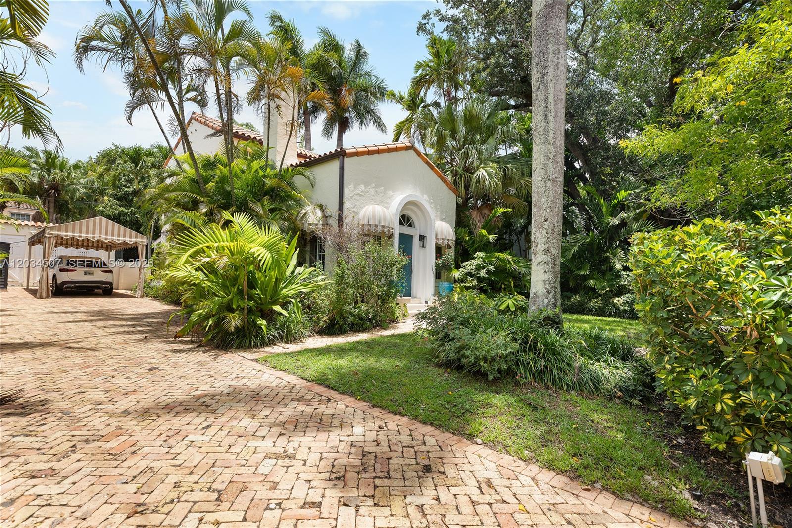 A white house with a brick driveway and lush tropical landscaping sits under a blue sky — 1511 SW 13th St, Miami FL 33145, MIAMI, FL