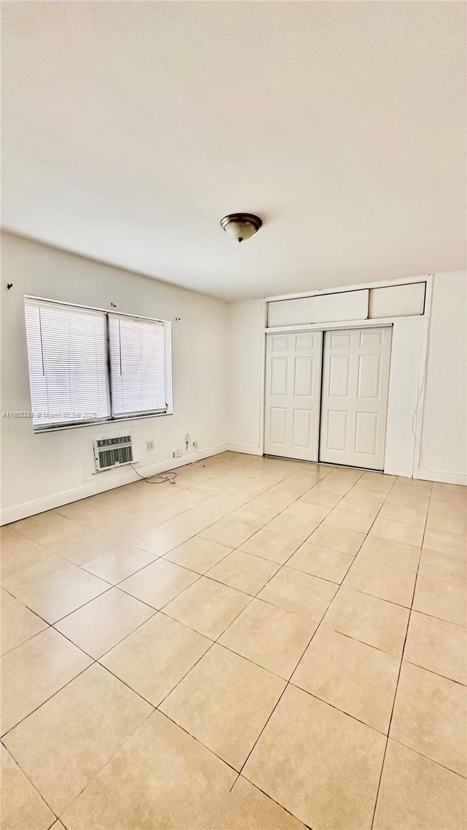 A bedroom features beige tile flooring, a window with blinds, and white closet doors — 1955 Normandy Dr # 2, Miami Beach FL 33141, MIAMI BEACH, FL