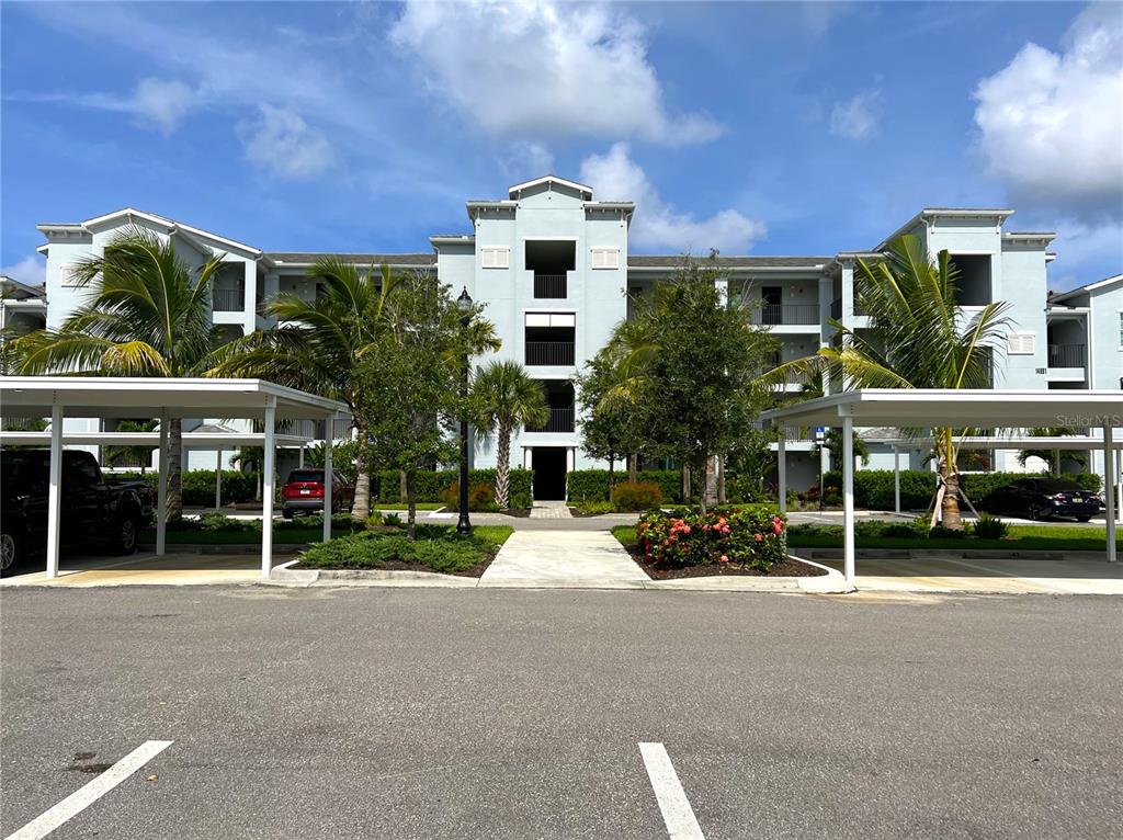 A multi-story apartment building with covered parking spaces and palm trees in the foreground — 14091 HERITAGE LANDING BOULEVARD UNIT 137, PUNTA GORDA, FL