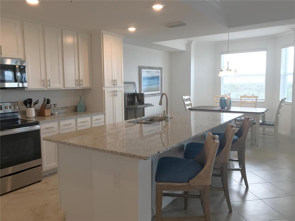 A kitchen with white cabinets, granite countertops, a large island, and an adjacent dining area — 14091 HERITAGE LANDING BOULEVARD UNIT 137, PUNTA GORDA, FL