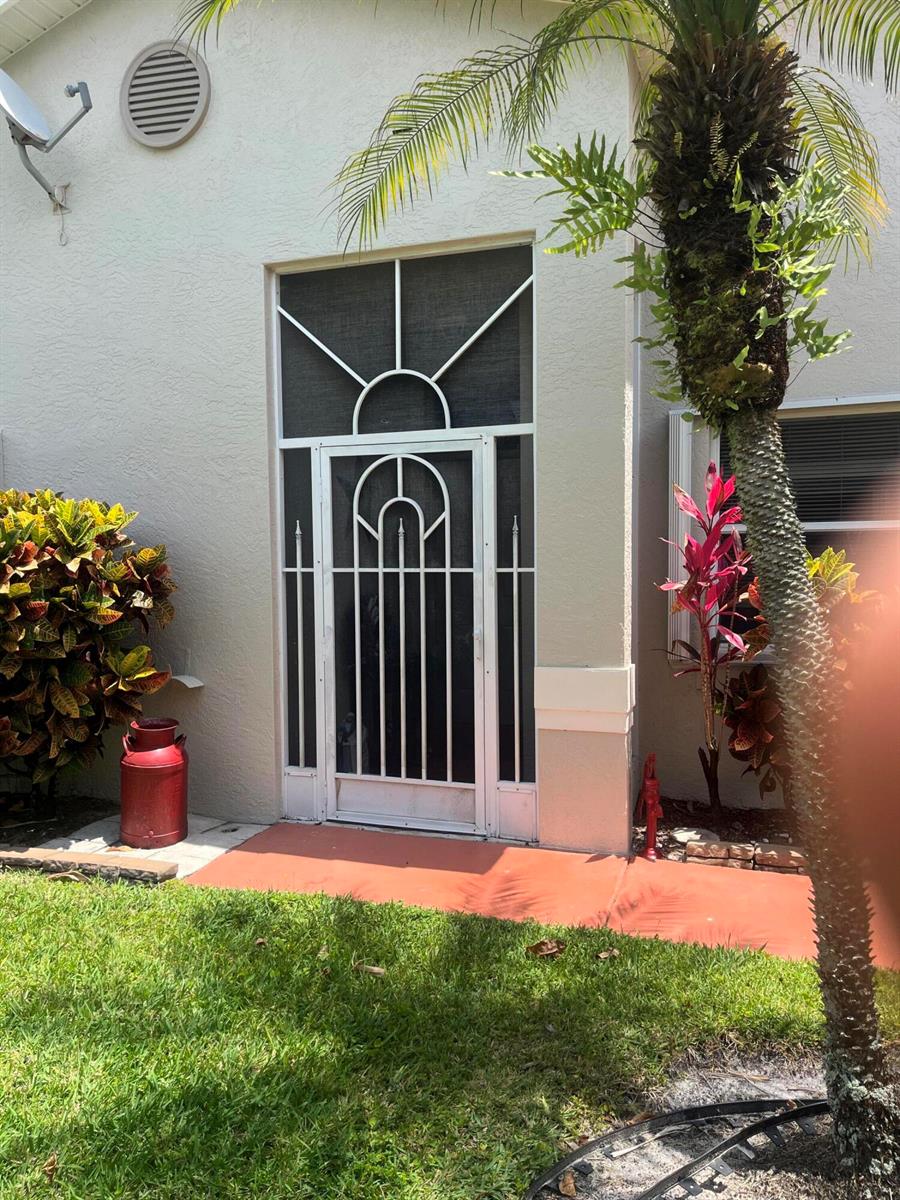 A white decorative screen door is centered on the exterior wall of a house — 96 Sausalito Circle, Boynton Beach FL 33436, BOYNTON BEACH, FL