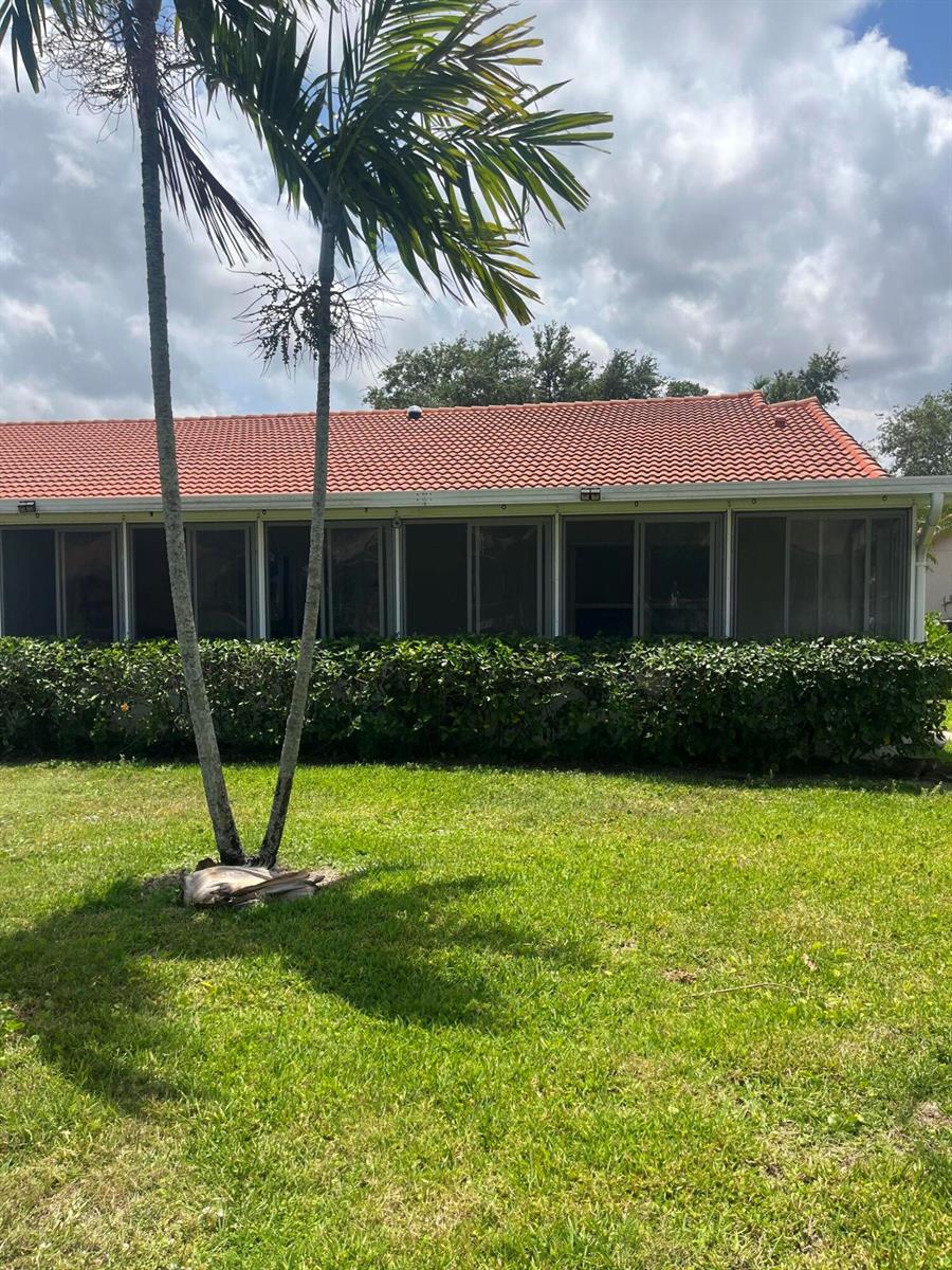 A view of a house exterior featuring a screened-in porch and a palm tree — 96 Sausalito Circle, Boynton Beach FL 33436, BOYNTON BEACH, FL