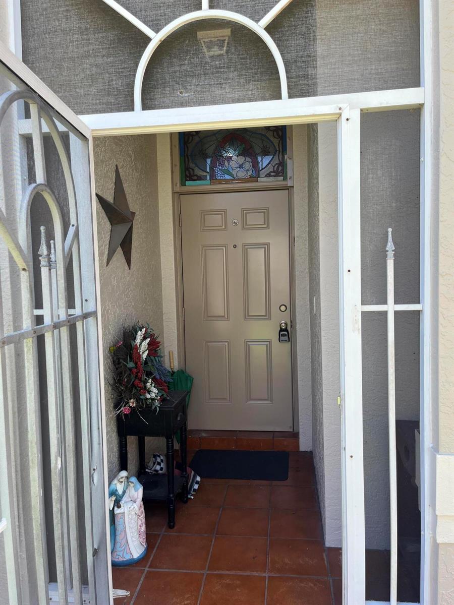 An entryway features a tan door with a stained glass transom and a metal screen door — 96 Sausalito Circle, Boynton Beach FL 33436, BOYNTON BEACH, FL