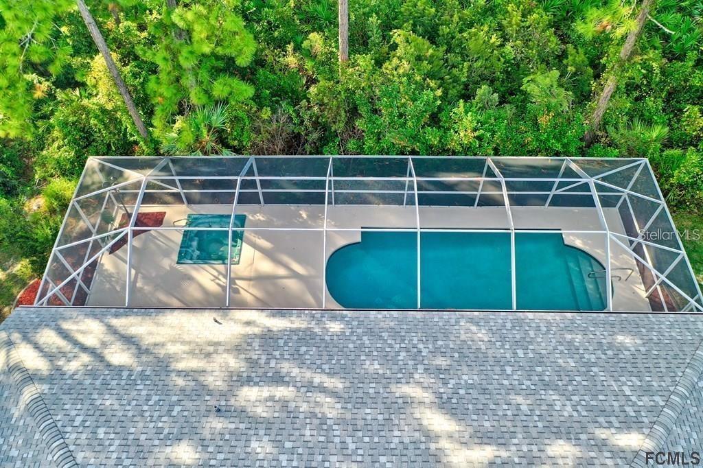 An aerial view shows a screened-in pool and spa area behind a shingled roof — 7 SHINNECOCK COURT, PALM COAST, FL