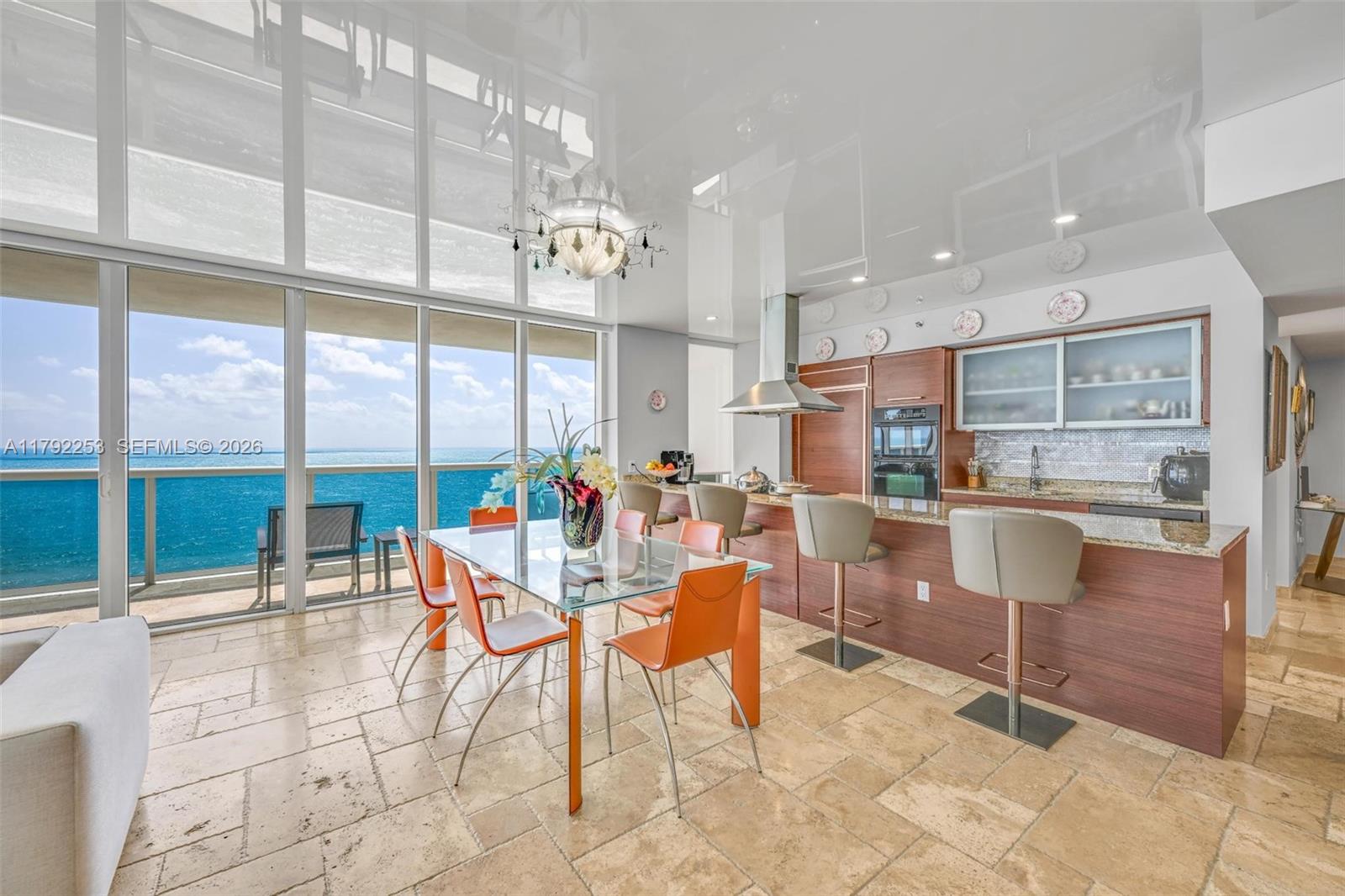 A modern kitchen and dining area feature a glass table, orange chairs, and ocean views — 1830 S Ocean Dr # 1201, Hallandale Beach FL 33009, HALLANDALE BEACH, FL
