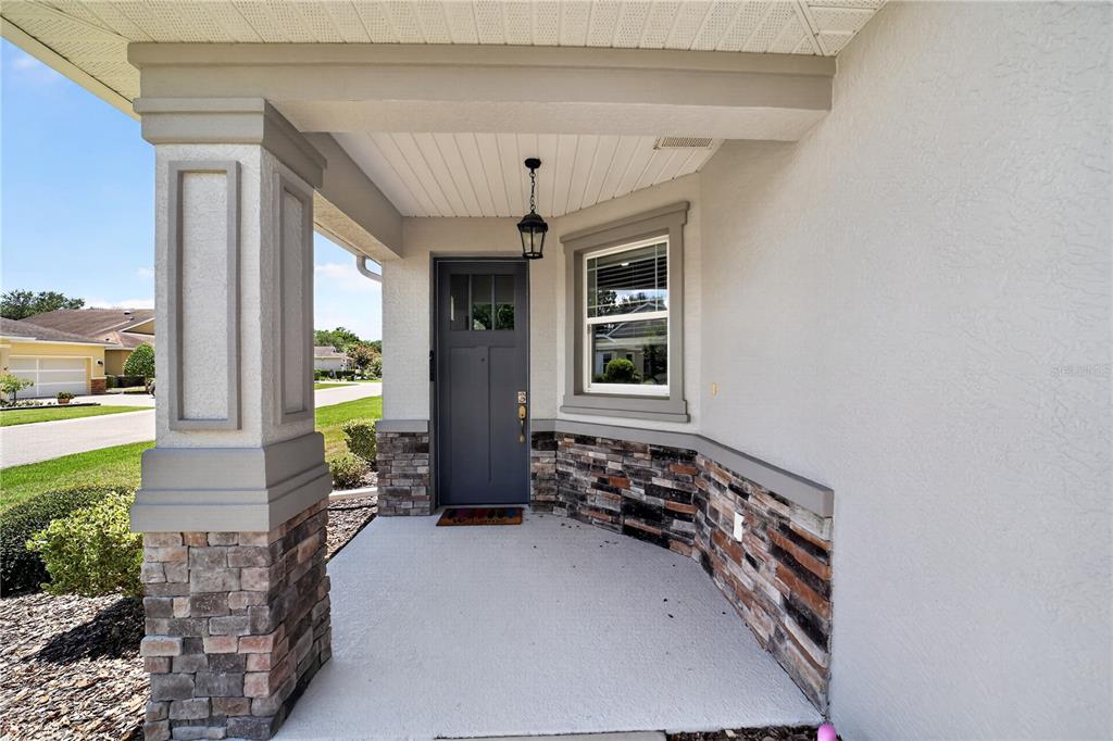 A covered front porch features a gray door, stone veneer accents, and a single hanging light — 9440 SW 98TH TERRACE, OCALA, FL