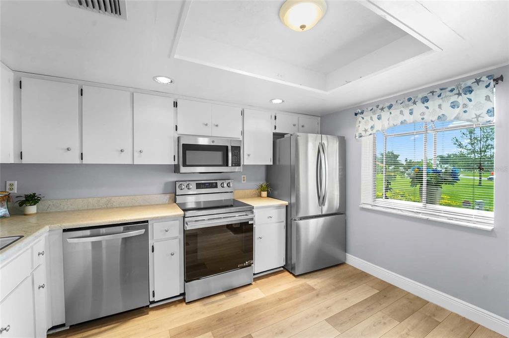 A kitchen featuring white cabinets, stainless steel appliances, light countertops, and wood-look flooring — 3351 STONEHAVEN COURT W UNIT C, PALM HARBOR, FL