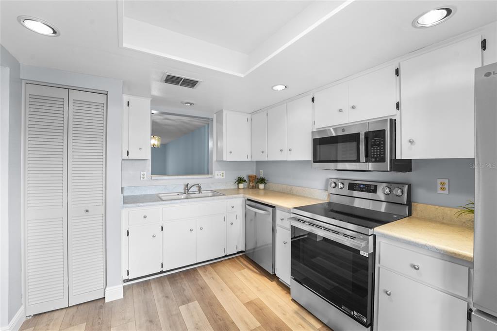 A kitchen with white cabinets, stainless steel appliances, light countertops, and wood-look flooring — 3351 STONEHAVEN COURT W UNIT C, PALM HARBOR, FL
