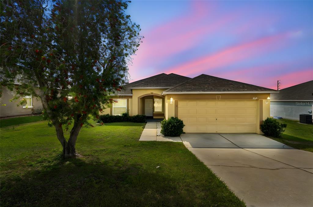 A single-story house with a yellow exterior, a two-car garage, and a front lawn — 7643 WEEHAWKEN DRIVE, ZEPHYRHILLS, FL