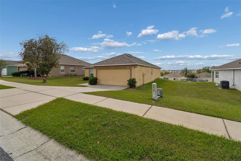 A tan single-story house with a two-car garage sits on a corner lot — 7643 WEEHAWKEN DRIVE, ZEPHYRHILLS, FL