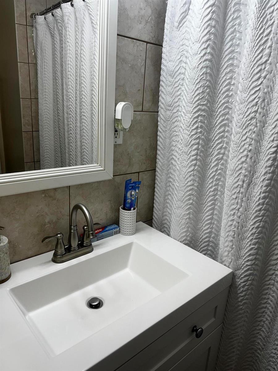 A bathroom features a white vanity with a sink, a mirror, and a textured shower curtain — 314 S L Street, FL 33460, FL
