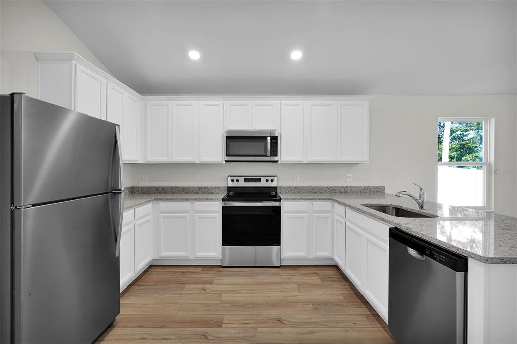 A kitchen with white cabinets, granite countertops, stainless steel appliances, and wood-look flooring — 5251 SW 164TH STREET ROAD, OCALA, FL
