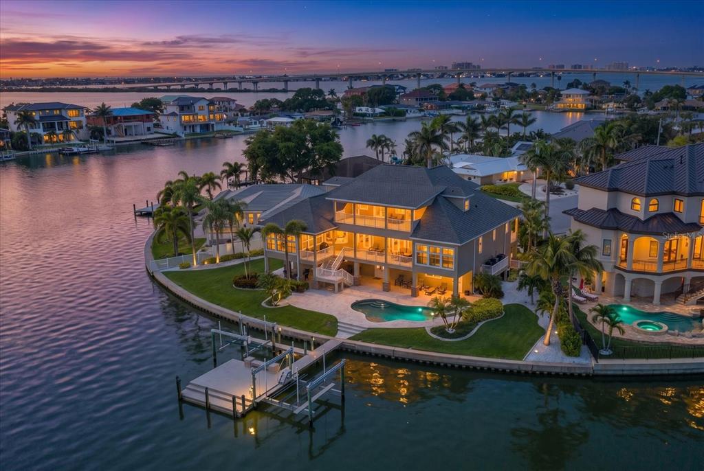 An aerial view of a multi-story waterfront home featuring a pool, dock, and sunset sky — 226 POINCIANA LANE, LARGO, FL