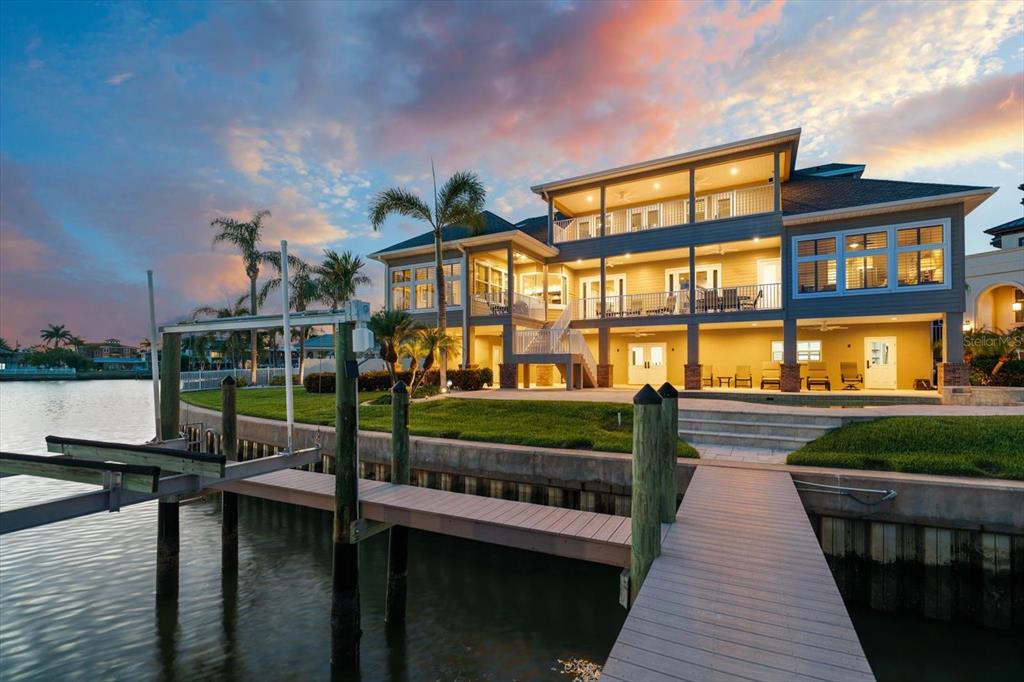 A multi-story waterfront house with a wooden dock and boat lift at sunset — 226 POINCIANA LANE, LARGO, FL
