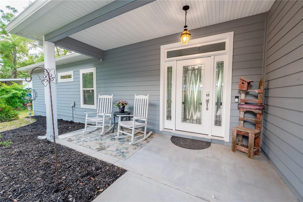 A covered front porch features gray siding, a white front door, and two white rocking chairs — 3709 NW 67TH TERRACE, BELL, FL