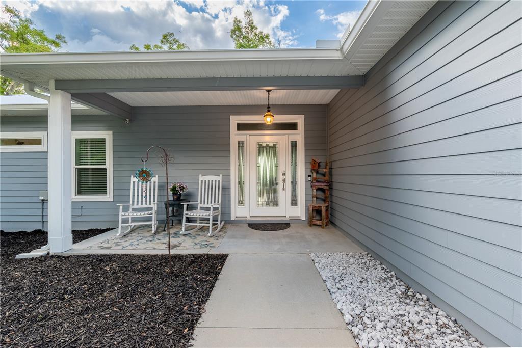 A covered front porch features gray horizontal siding, a white front door, and two rocking chairs — 3709 NW 67TH TERRACE, BELL, FL