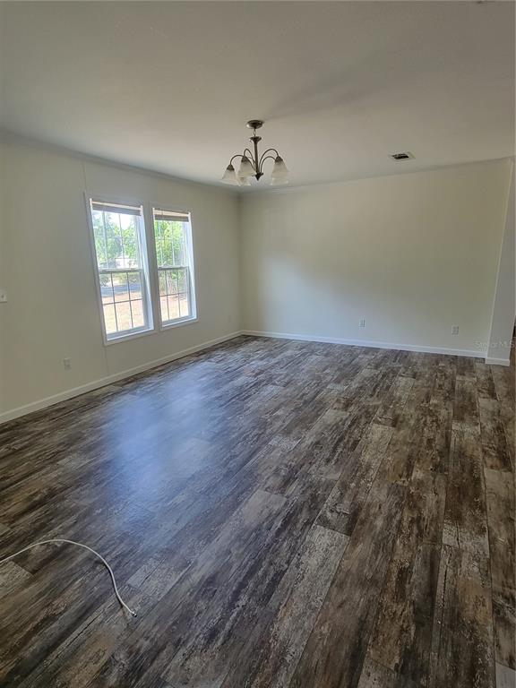 An empty room features light-colored walls, a chandelier, and dark wood-look plank flooring — 2435 MYER AVENUE, LEESBURG, FL