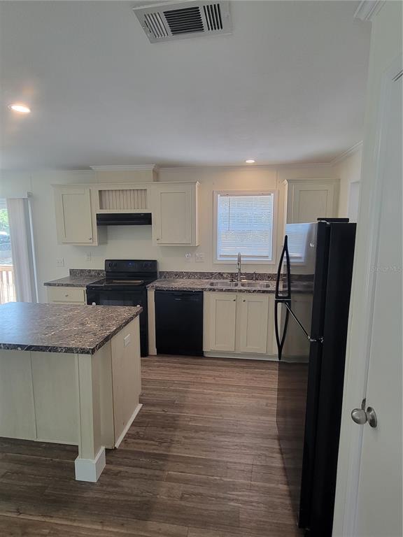 A kitchen features cream cabinets, dark countertops, a kitchen island, and black appliances — 2435 MYER AVENUE, LEESBURG, FL