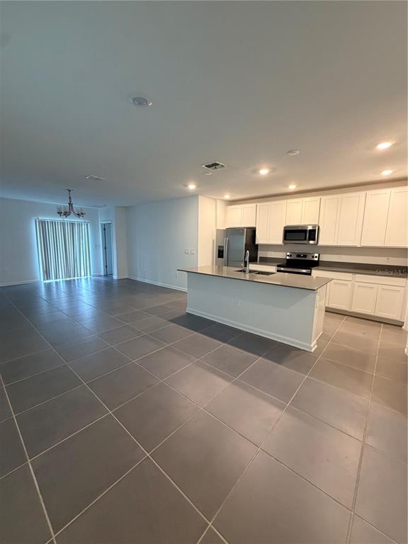 A kitchen with white cabinets and a center island opens to a tiled living area — 926 JACKSON AVENUE, DAVENPORT, FL