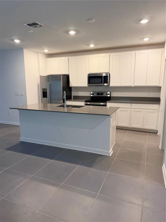 A kitchen features white cabinets, stainless steel appliances, a gray island, and tiled flooring — 926 JACKSON AVENUE, DAVENPORT, FL
