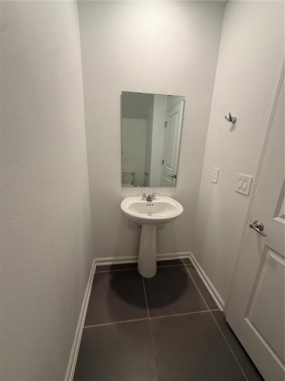 A small bathroom features a white pedestal sink, a wall mirror, and dark floor tiles — 926 JACKSON AVENUE, DAVENPORT, FL