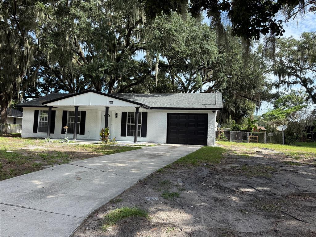 A single-story white brick house with black shutters and a garage under large oak trees — 3008 OAKVIEW LANE, PLANT CITY, FL