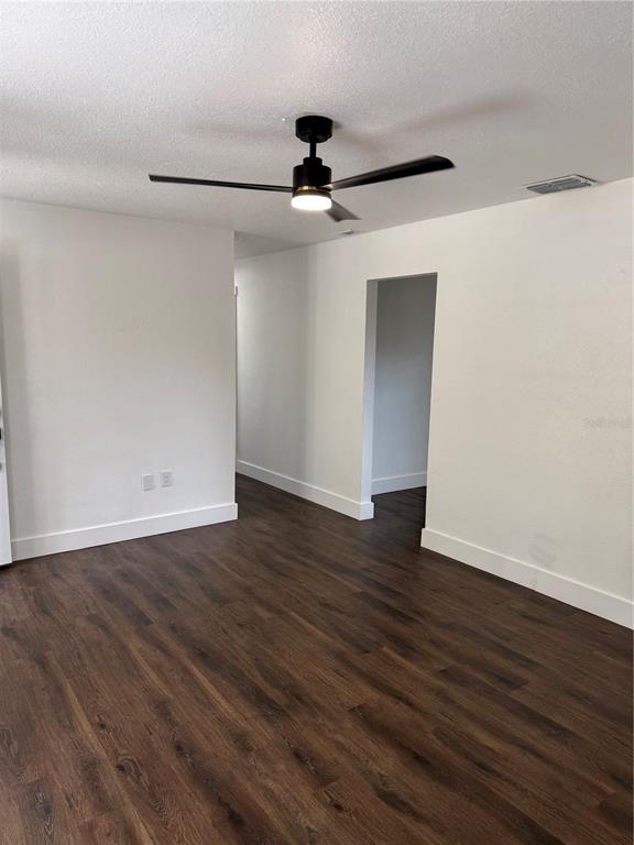 An empty room features dark wood-look flooring, white walls, and a modern black ceiling fan — 3008 OAKVIEW LANE, PLANT CITY, FL