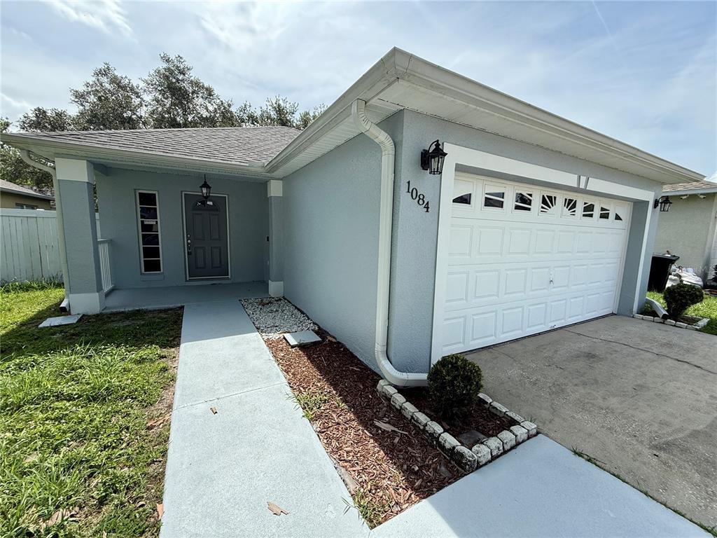A light blue house exterior features a white garage door, a front porch, and walkway — 1084 AMANDA KAY CIRCLE, SANFORD, FL