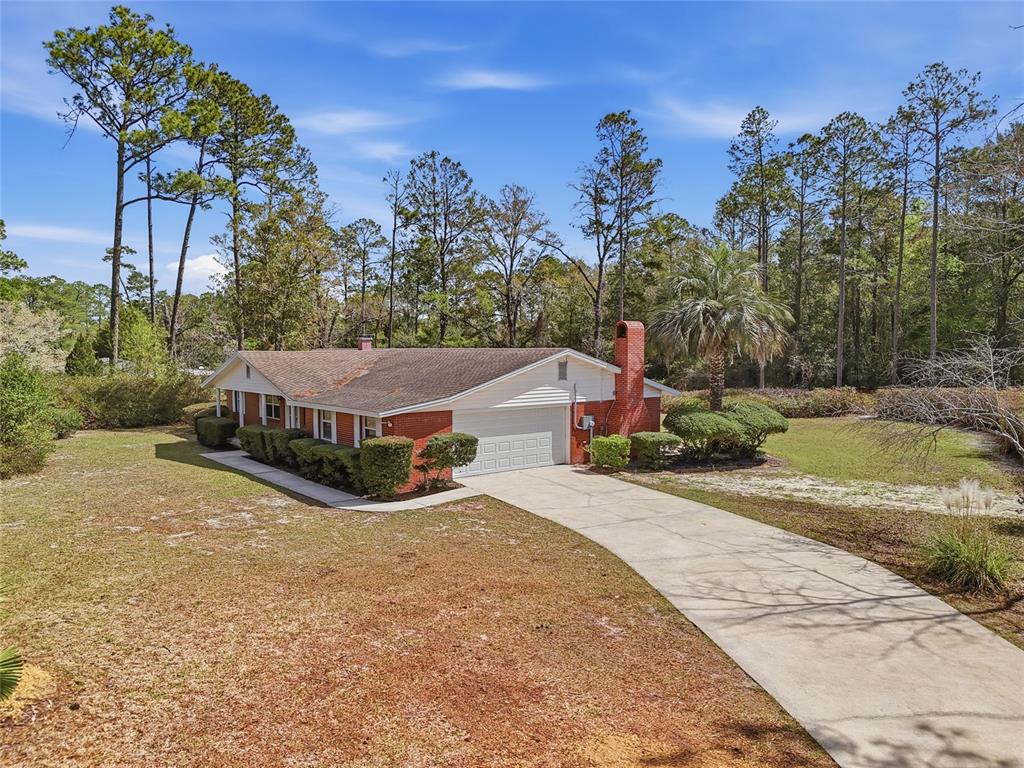 A single-story brick house with a white garage door sits on a large grassy lot — 129 SW BENZ WAY, LAKE CITY, FL