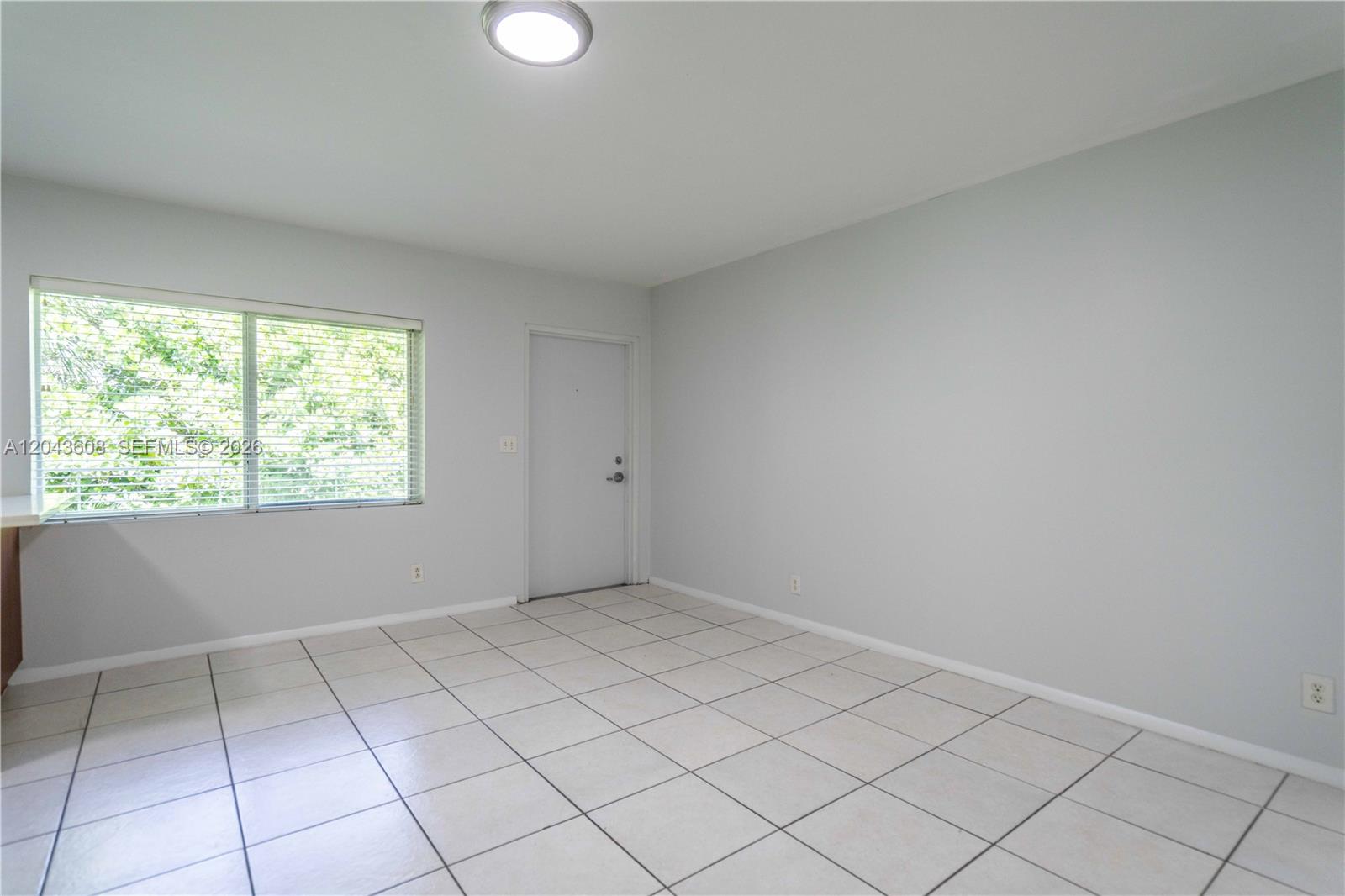 An empty room features light gray walls, white tile flooring, a window, and a door — 666 NE 80th St # 8, Miami FL 33138, MIAMI, FL
