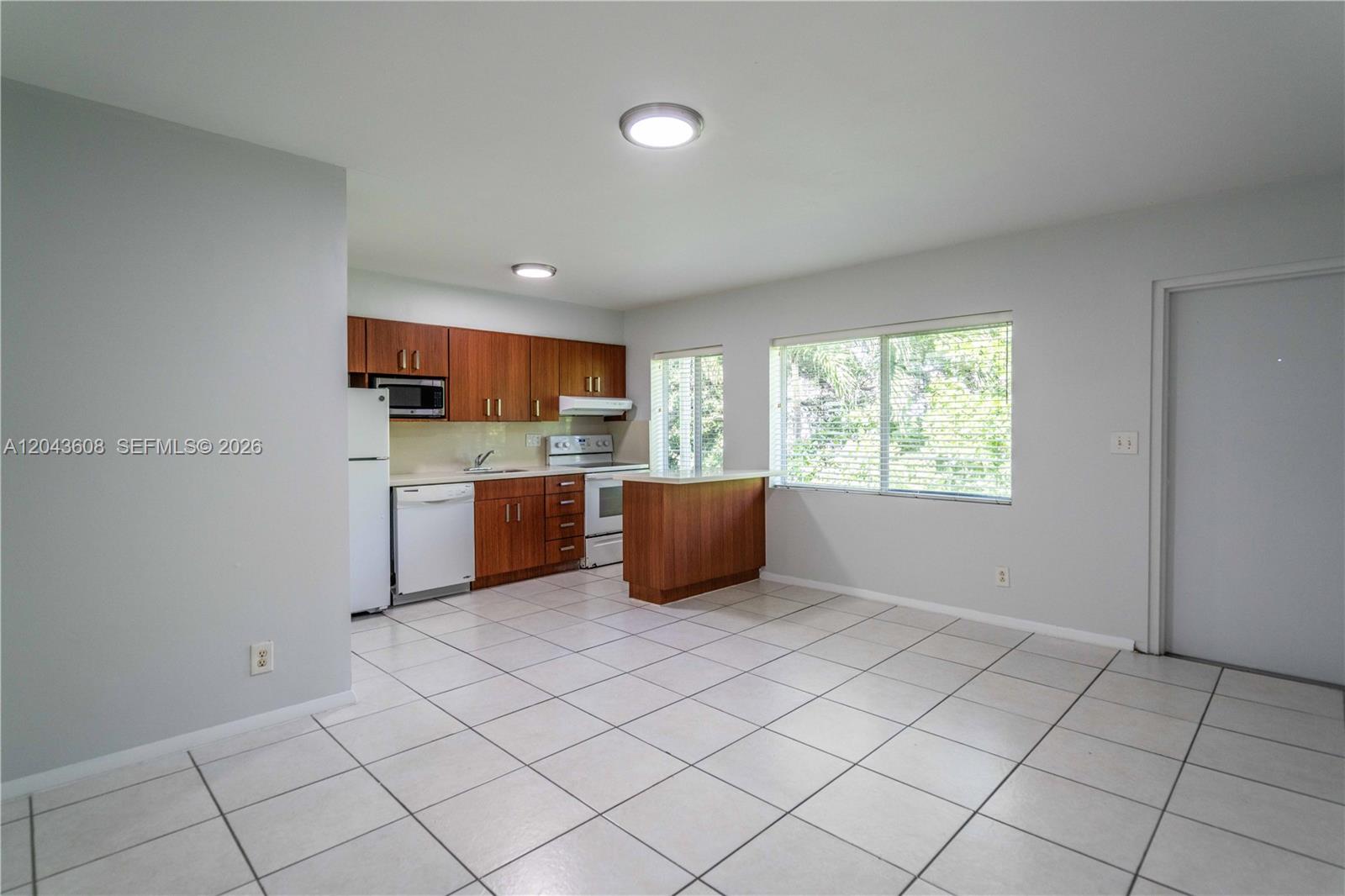 A kitchen with wood cabinets, white appliances, and tile flooring opens to a dining area — 666 NE 80th St # 8, Miami FL 33138, MIAMI, FL