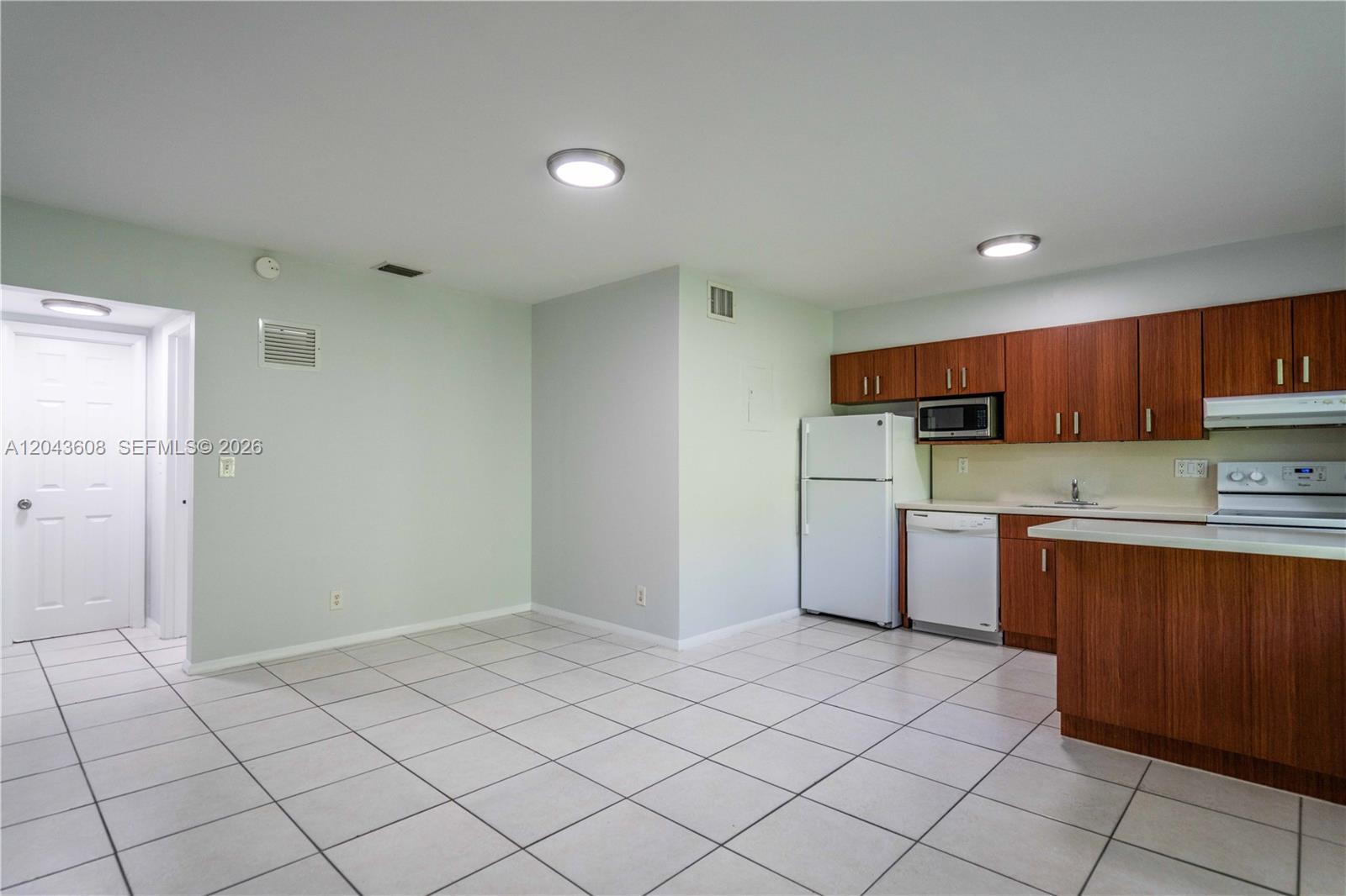 A kitchen with wood cabinets, white appliances, and light tile flooring opens to a dining area — 666 NE 80th St # 8, Miami FL 33138, MIAMI, FL