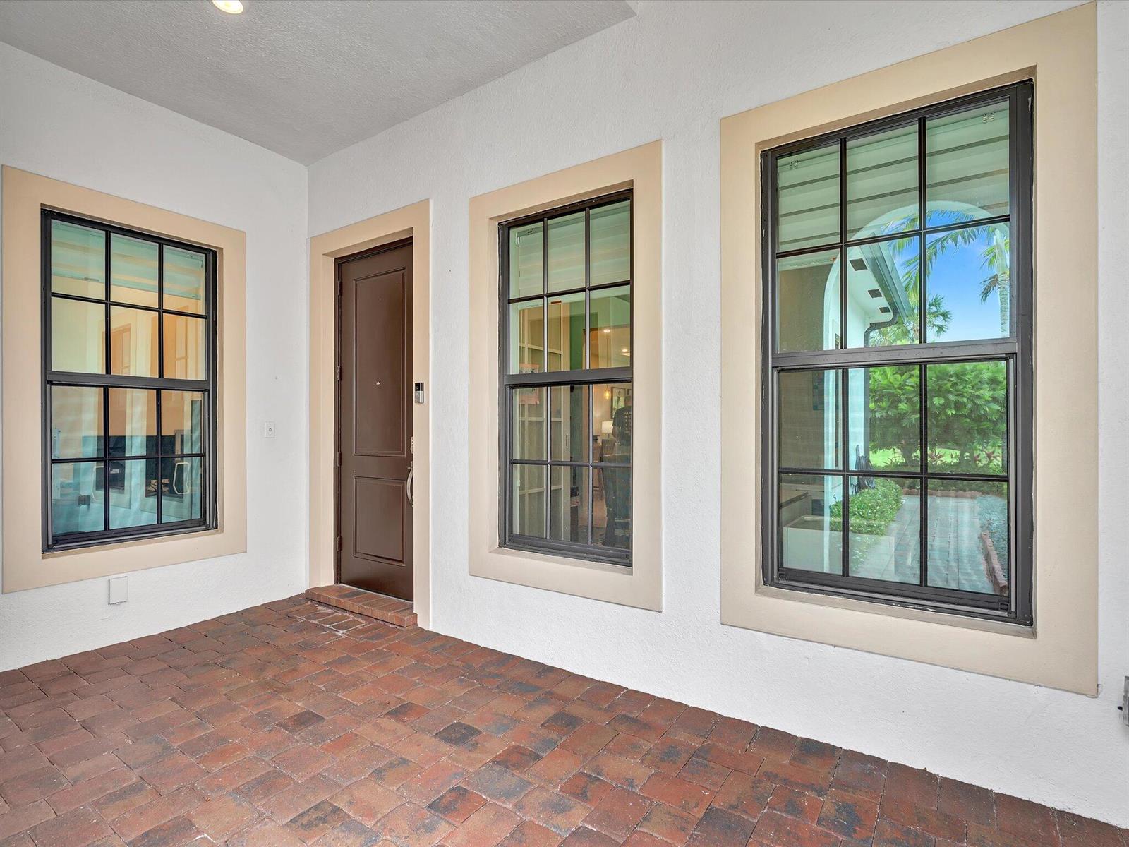 A covered patio with brick pavers features a brown door flanked by three large windows — 7457 S Blue Spring Drive, Parkland FL 33067, PARKLAND, FL