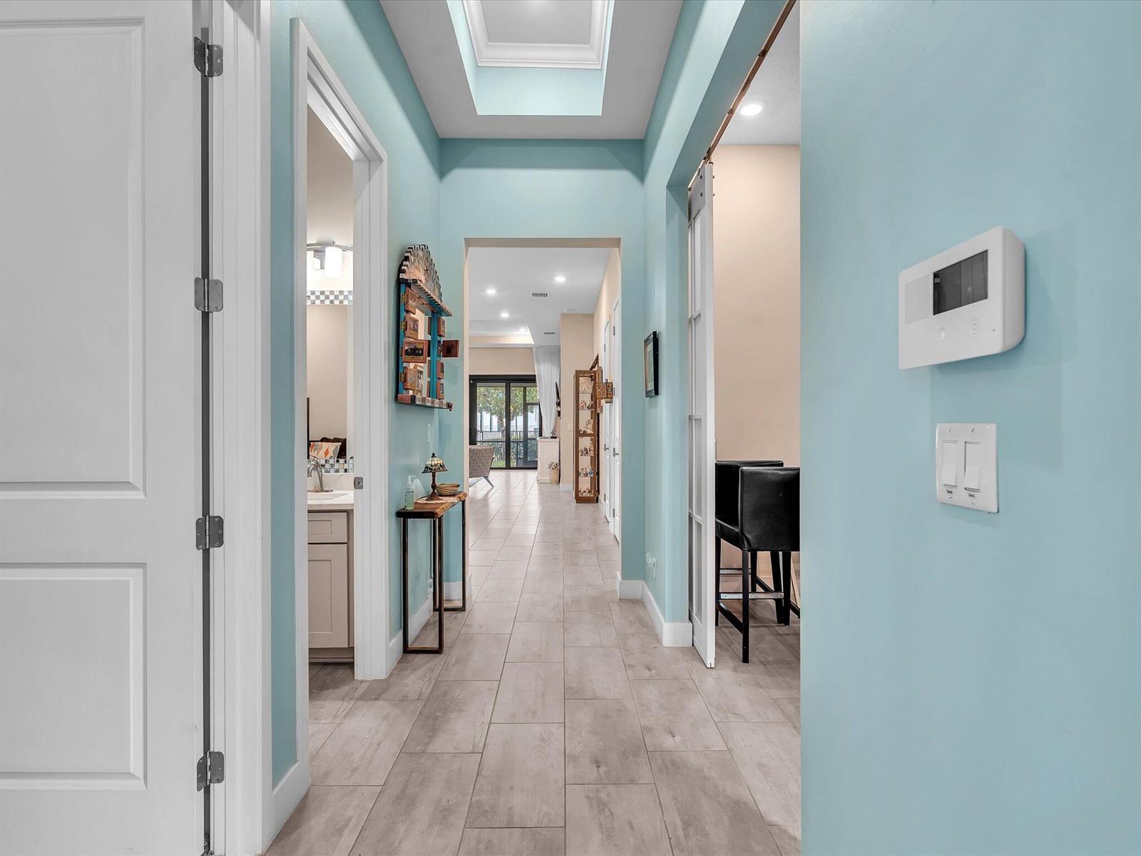 A light blue hallway with tile flooring leads toward an open living area with glass doors — 7457 S Blue Spring Drive, Parkland FL 33067, PARKLAND, FL