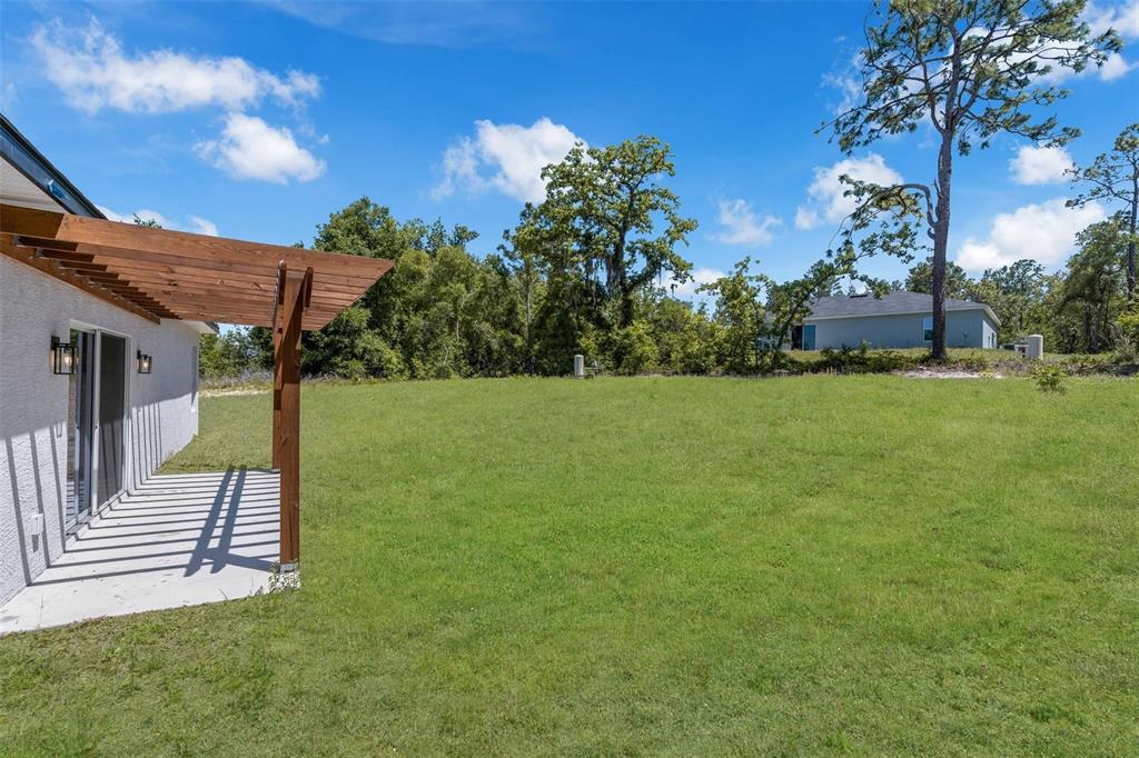 A wooden pergola extends over a concrete patio next to a grassy backyard — 2386 SW 168TH LOOP, OCALA, FL