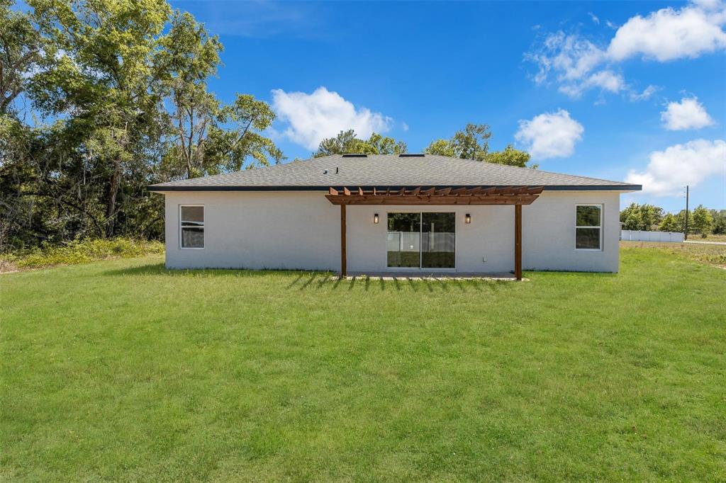 The rear exterior of a single-story house features a wooden pergola over a sliding door — 2386 SW 168TH LOOP, OCALA, FL