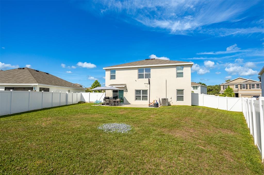 The backyard of a two-story house features a patio, white vinyl fencing, and grass — 13688 WINEBERRY DRIVE, DADE CITY, FL